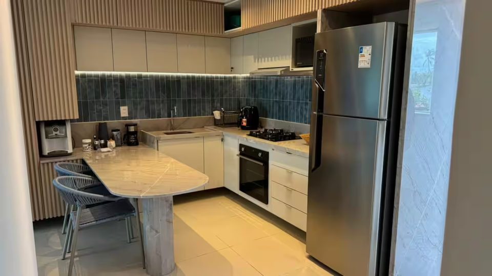 Cozinha equipada do 302D com geladeira inox, forno, cooktop e bancada com banquetas.