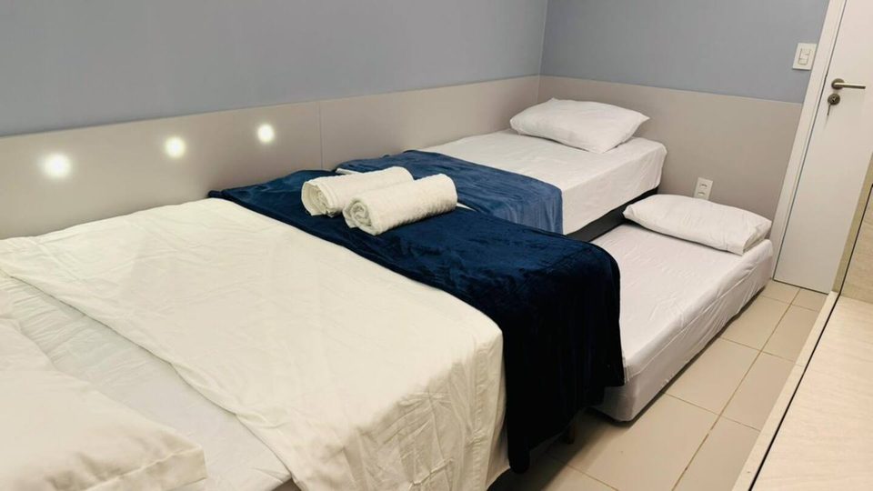 Quarto do 302D com duas camas de solteiro, cabeceira iluminada e toalhas dobradas.