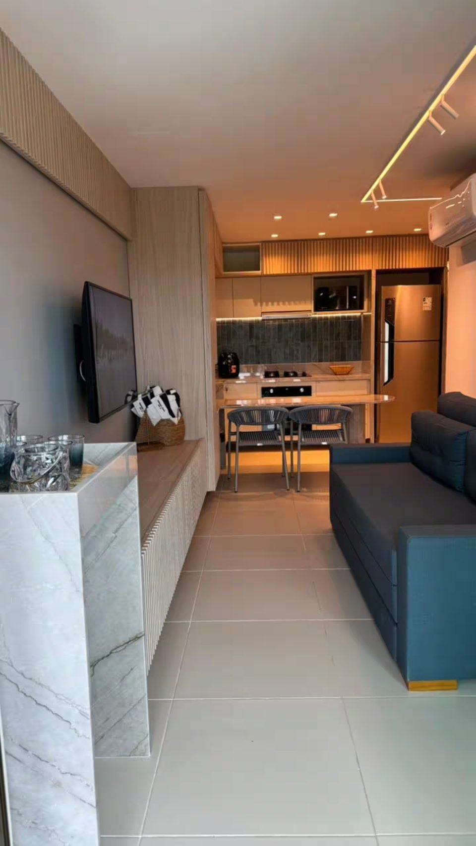 Sala integrada à cozinha americana do 302D, com sofá, televisão e bancada de mármore.