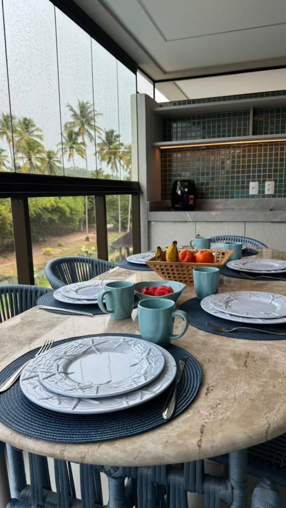 Mesa posta na varanda do 302D com café da manhã e coqueiros ao fundo.