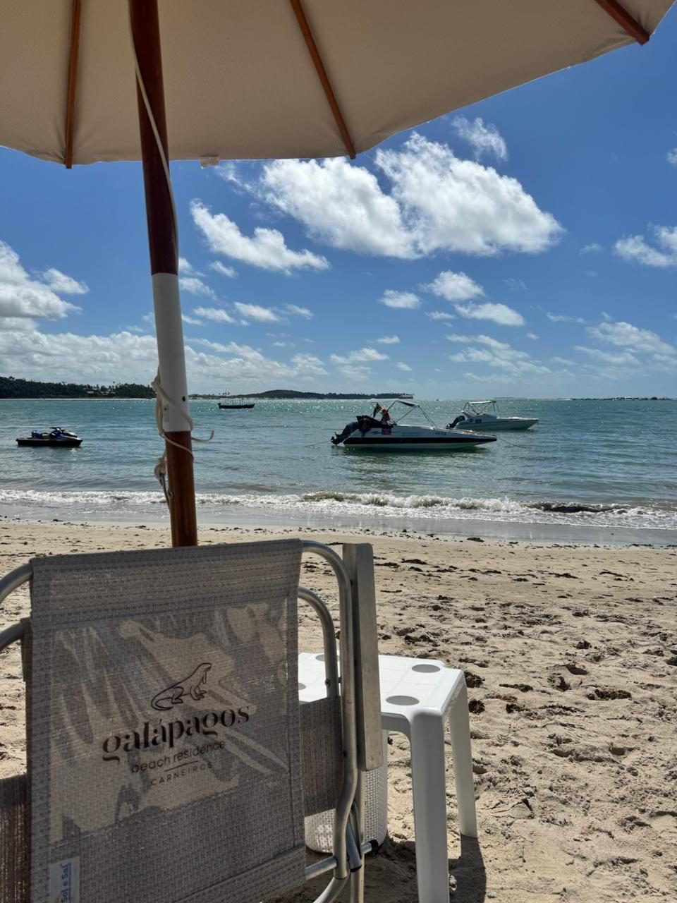 Cadeira de praia com a marca Galápagos sob um guarda-sol, de frente para o mar.