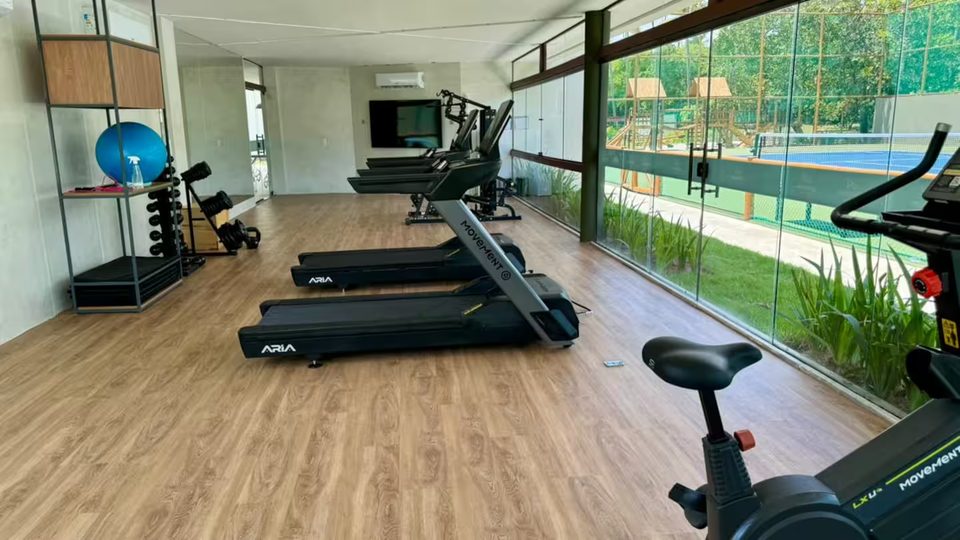 Academia do condomínio com esteiras e bicicletas voltadas para a piscina.