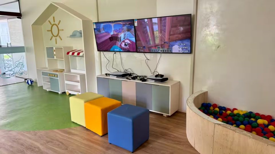 Brinquedoteca do condomínio com televisão, piscina de bolinhas e brinquedos de madeira.