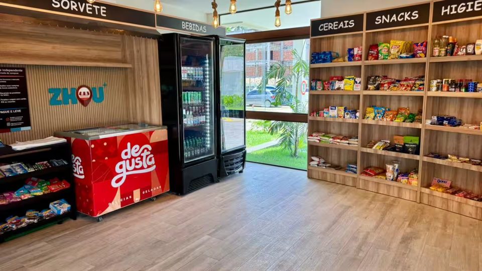 Mini market do condomínio com prateleiras de mantimentos e geladeira de bebidas.