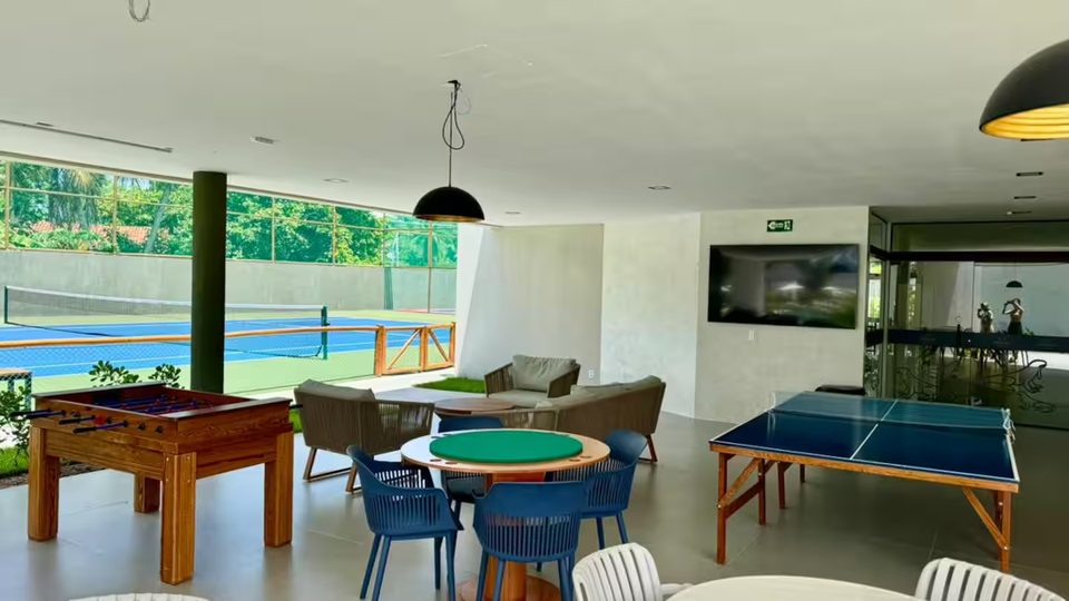 Salão de jogos do condomínio com mesa de sinuca, tênis de mesa e vista para a piscina.